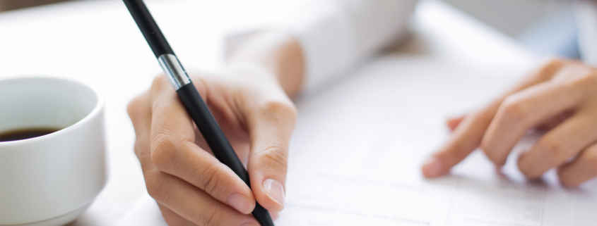 Close up of a woman going over paperwork at a table with a cup of coffee by her hand