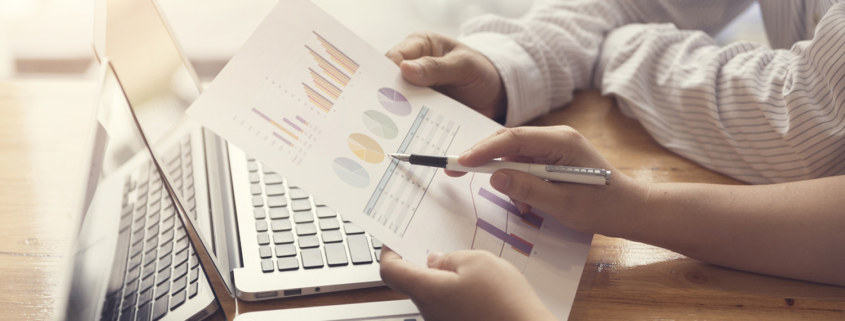 employees look over charts with their laptops open in the bg