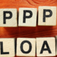 Tiles with PPP LOAN spelled out on a desk with office accessories